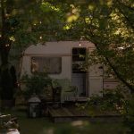 white and green rv trailer under green tree during daytime