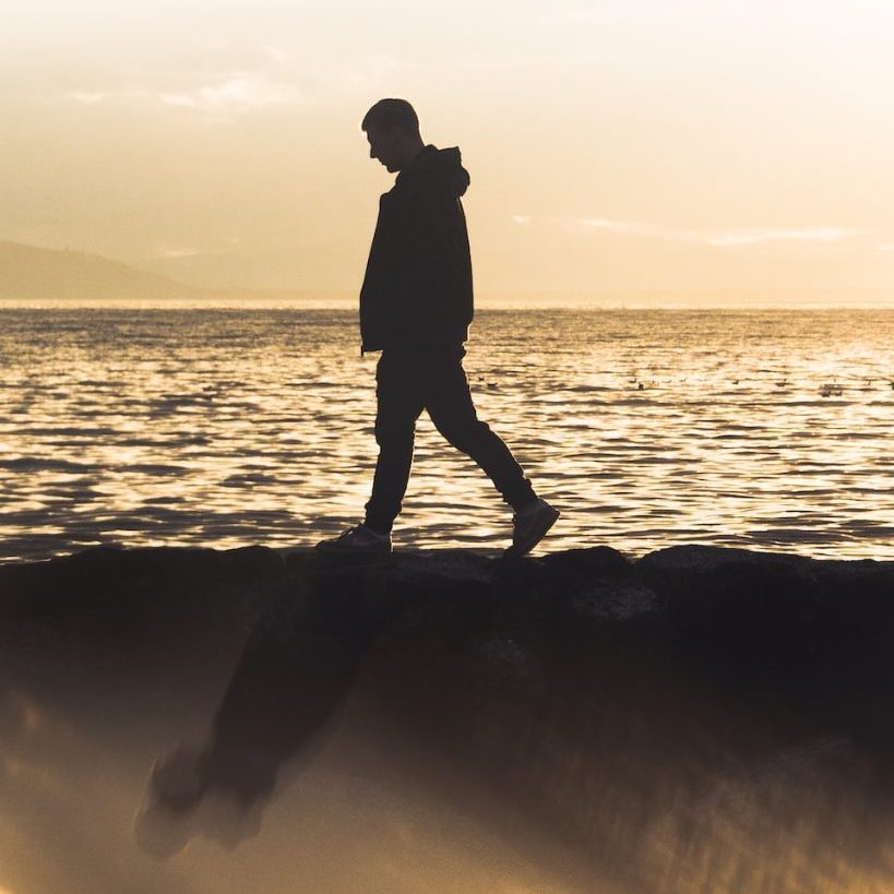 silhouette of man standing on rock near sea during sunset